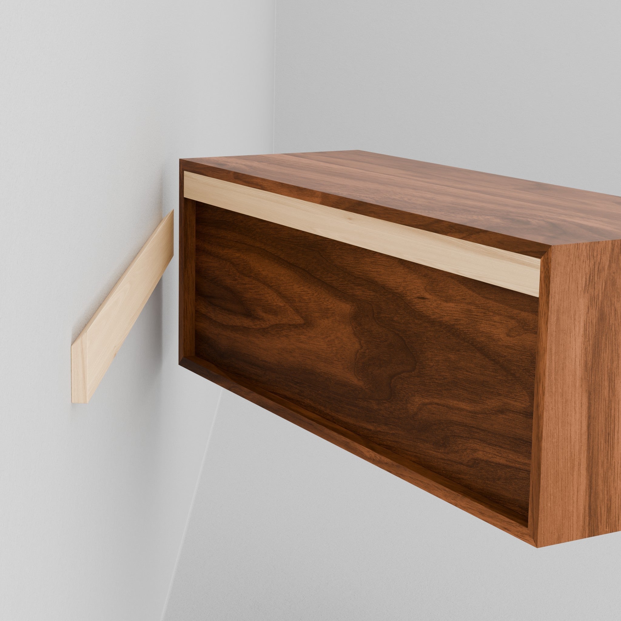 A person aligns a Krovel Hardwood Floating Display Case, featuring a French cleat, with a matching wall-mounted cleat on a white wall, preparing to hang the cabinet.