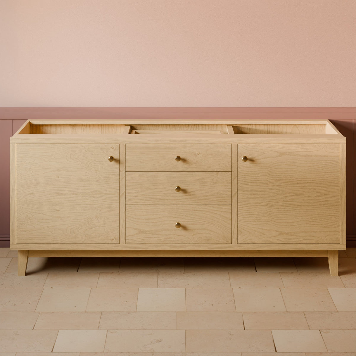 A light natural oak wood sideboard or credenza with three drawers in the center and two cabinet doors on the sides, accented with small round brass knobs, set against a pink and beige wall with tiled flooring.#wood_maple