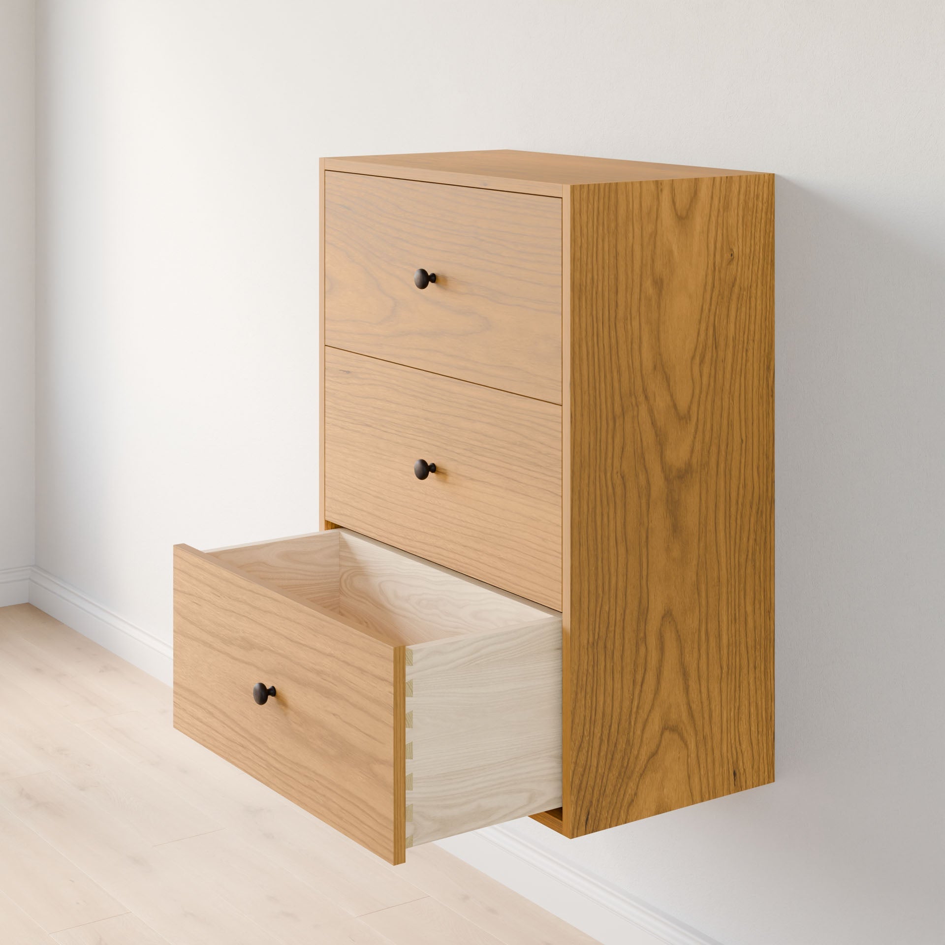The Maine Made Closet Drawers by Krovel Furniture Co. is a wall-mounted wooden dresser with three drawers, crafted from premium cabinet plywood, featuring a modern design with black round knobs and an open bottom drawer displaying a light interior.