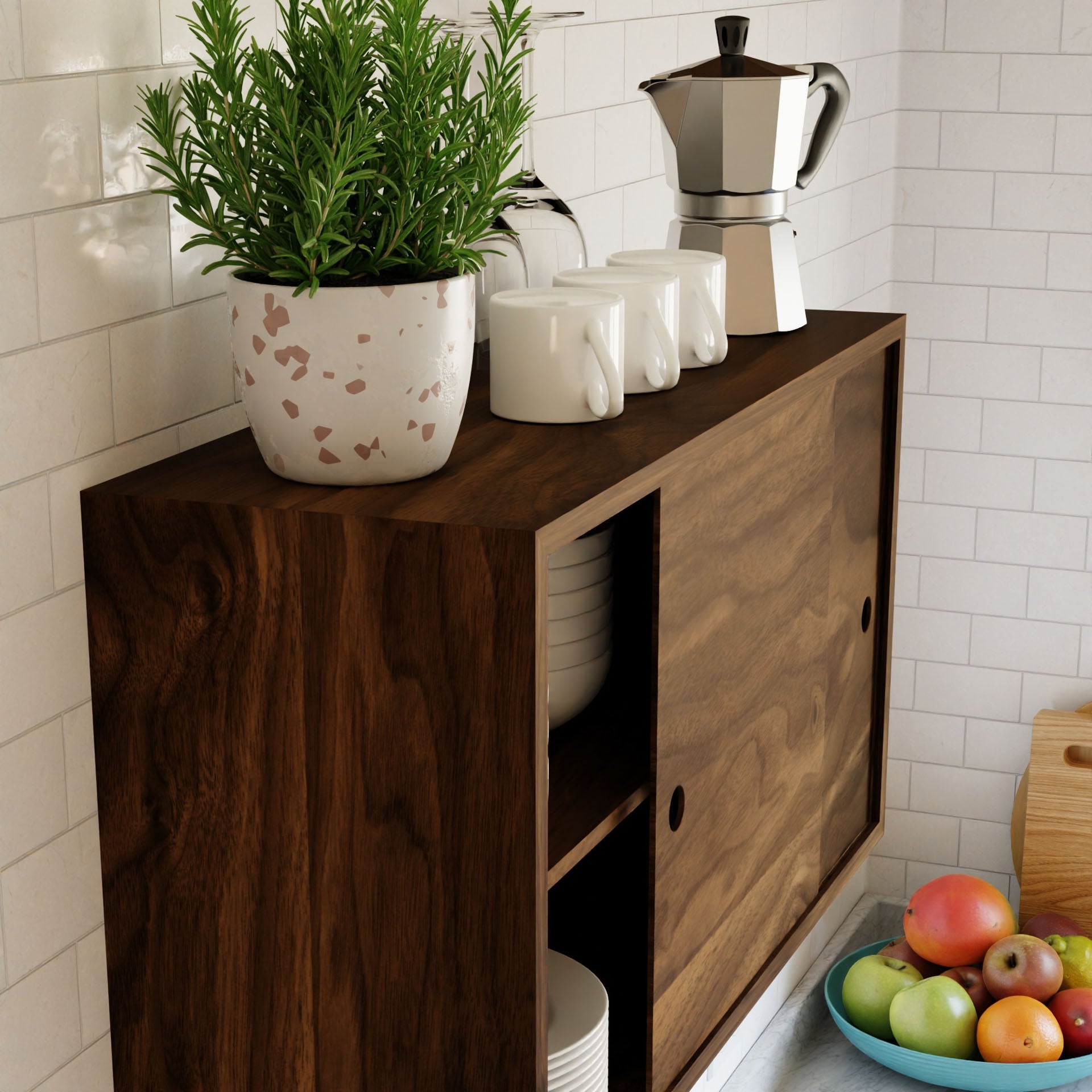 A kitchen scene showcases a Krovel Cupboard with Shelf in Walnut, adorned with a potted plant, ceramic mugs, and a stovetop espresso maker on its surface. Inside the cupboard, plates are neatly arranged. Nearby, a bowl filled with vibrant fruits—apples and peaches—enhances the cozy atmosphere.