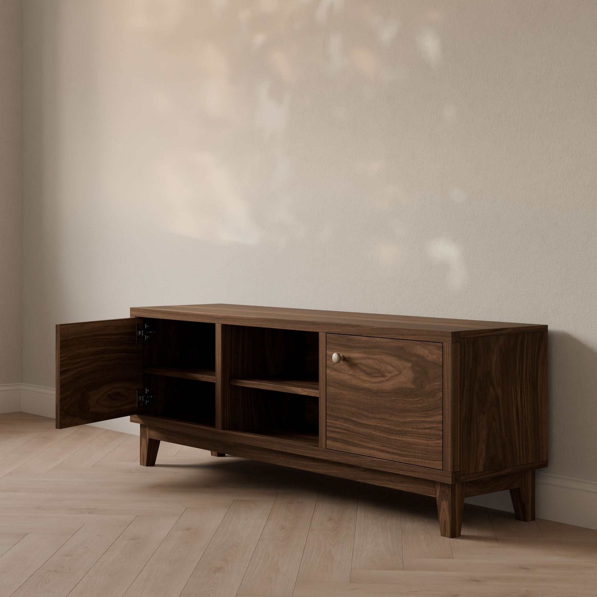 The Maine Made Double Door, Open Shelf Media Cabinet by Krovel Furniture Co. is a customizable, formaldehyde-free wooden sideboard with mid-century design, featuring one open left door and one closed right door on a light wood floor against a beige wall.