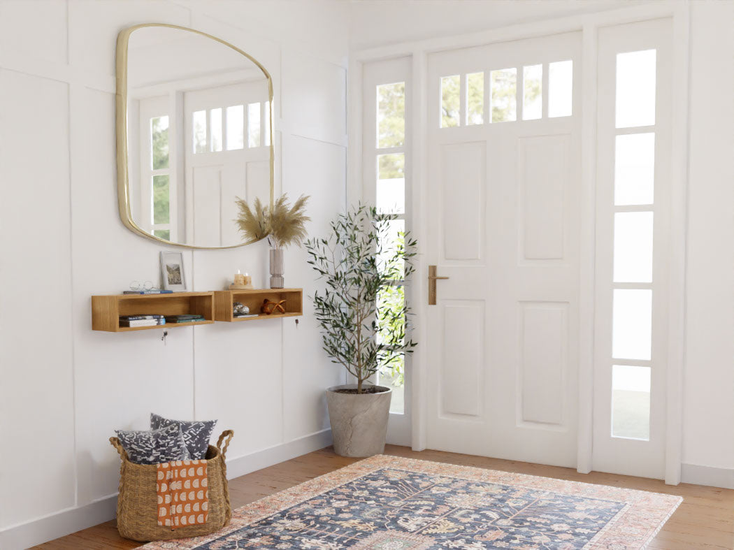A bright, minimalist entryway features an Entryway Organizer in White Oak by Krovel, alongside an American White Oak door with glass panels. This stylish space includes a large mirror, a wooden shelf adorned with decor items, a potted plant, and a woven basket filled with cushions on a patterned rug. The floating organizer provides both elegance and practicality.