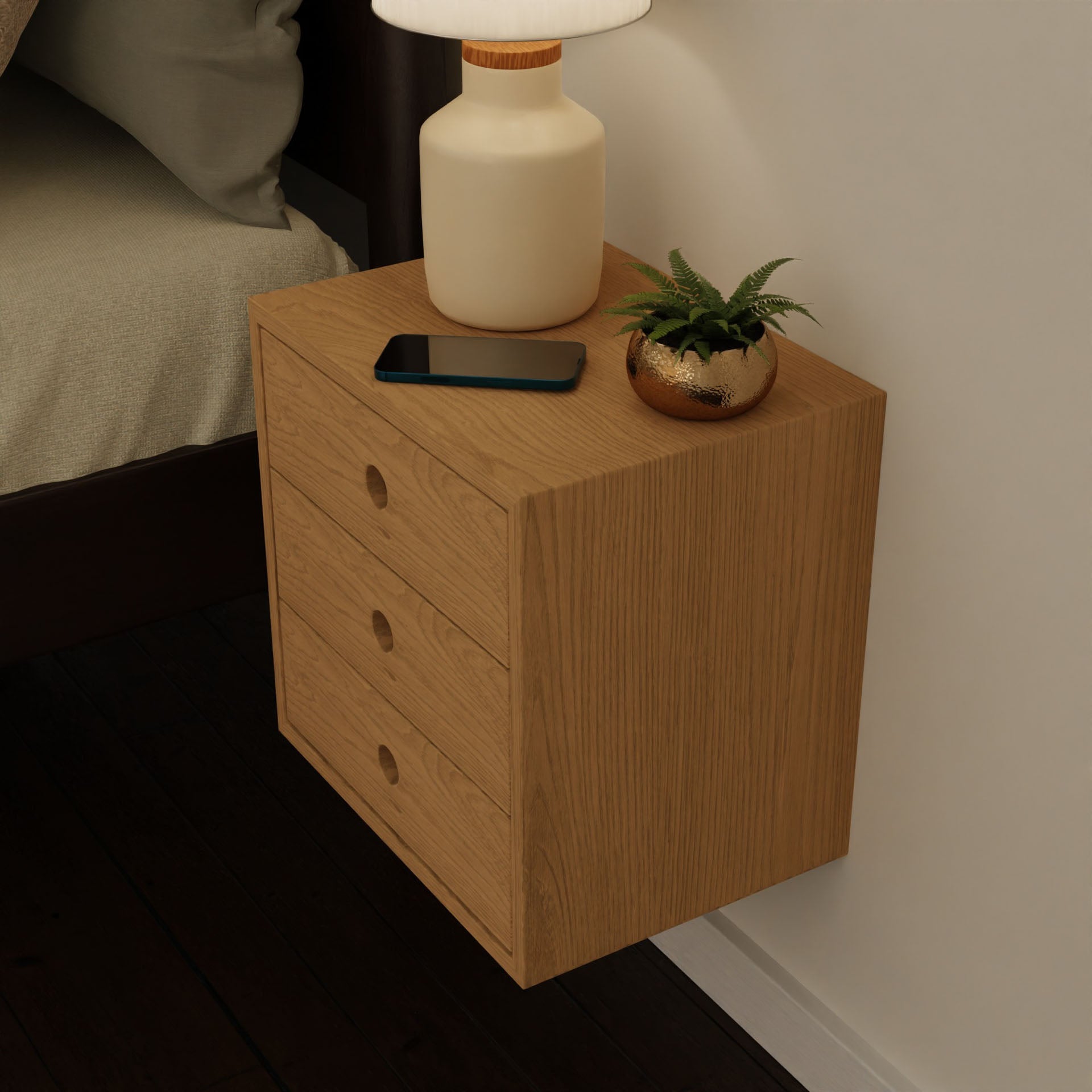 The Krovel Hardwood Triple Floating Nightstand, made from solid hardwood, features three drawers and holds a lamp, gold potted plant, and smartphone next to a bed with beige bedding.