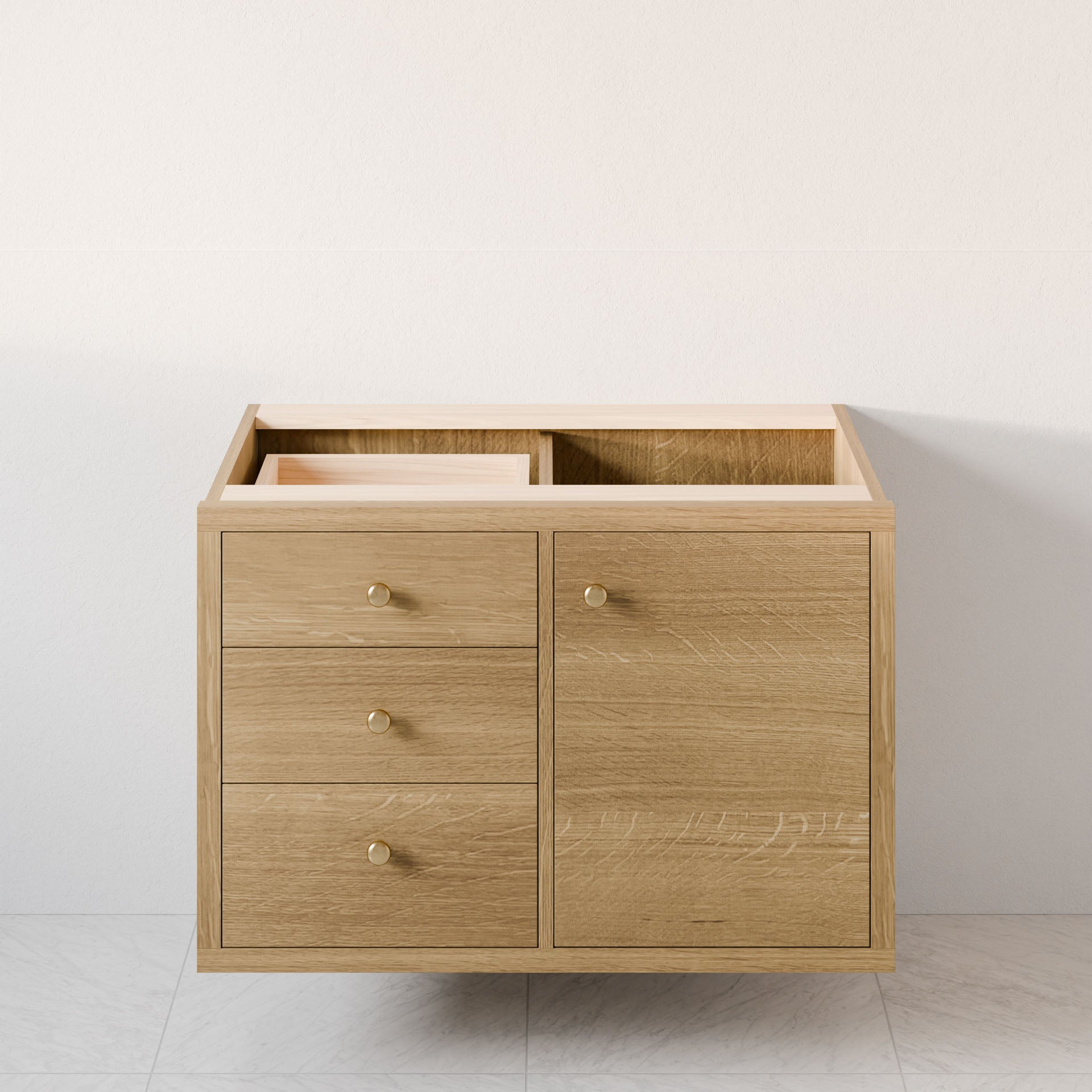 The Maine Made Single Door, Triple Drawer Vanity by Krovel Furniture Co. stands against a light wall on a pale tiled floor. This hardwood single-sink vanity has three left drawers, one right cabinet door with round golden knobs, and no countertop.