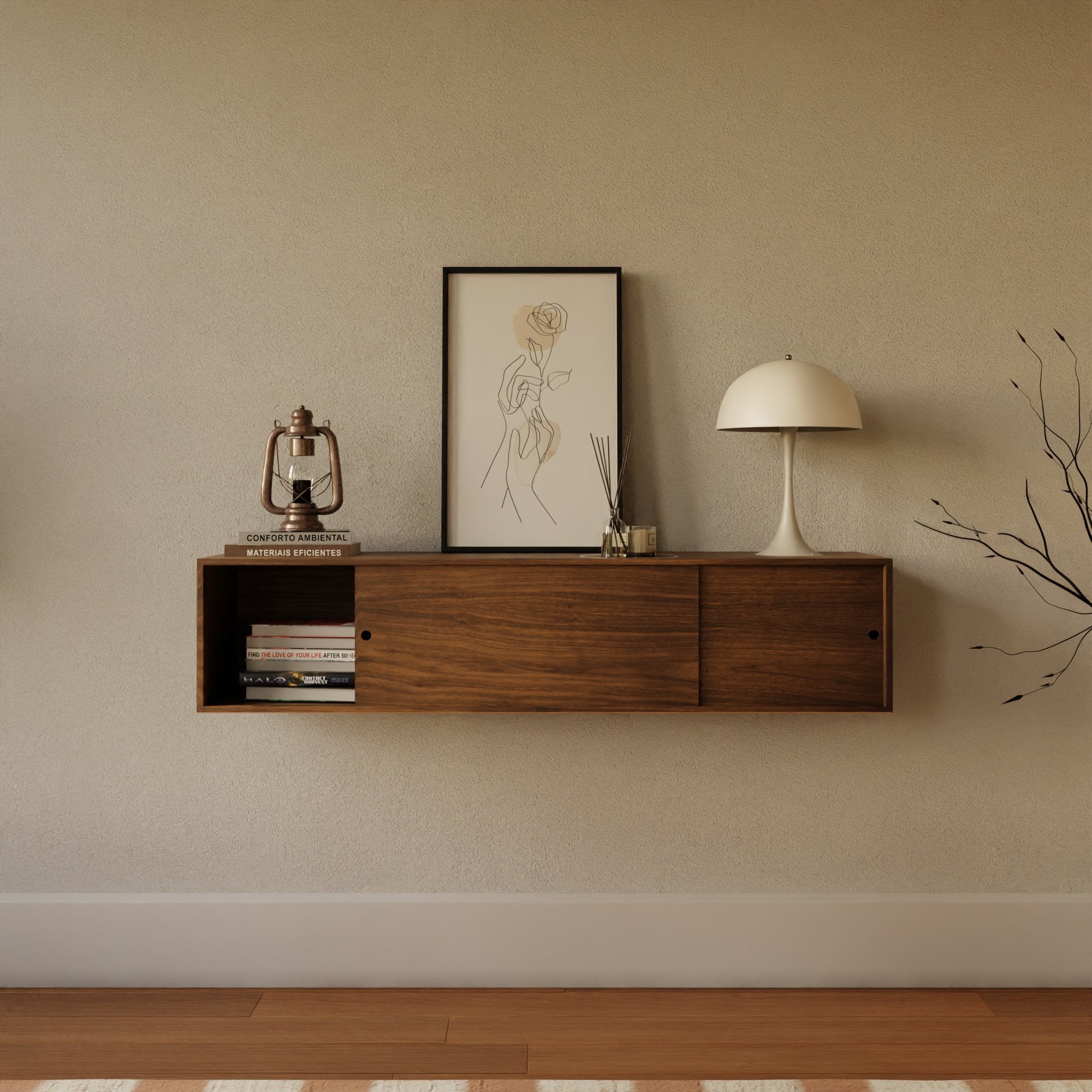 A minimalist wall-mounted wooden shelf holds a framed line drawing, a vintage lantern, books, a reed diffuser, and a modern lamp. A bare branch decoration leans against the light-colored wall.