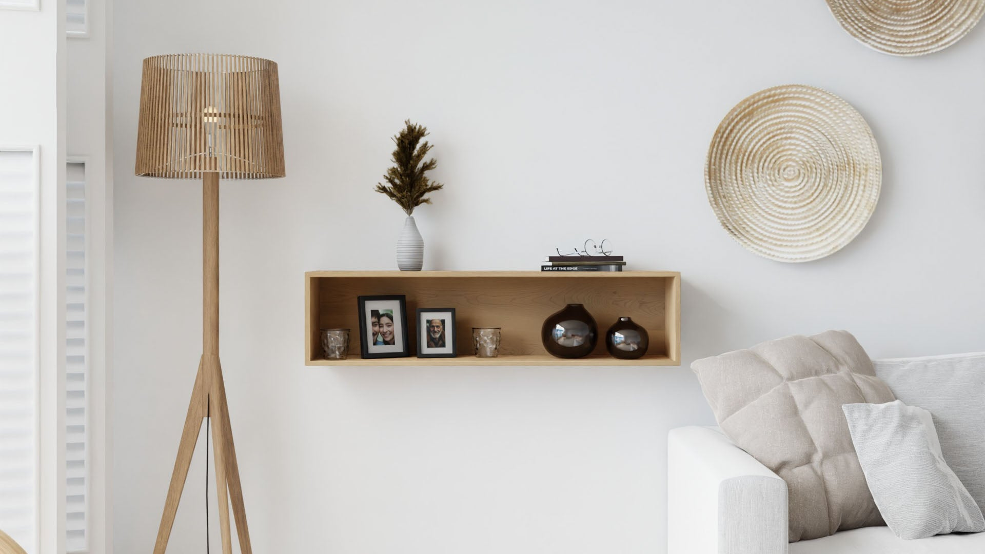 A modern living room with a wooden floor lamp, a floating shelf holding framed photos, vases, and books, woven wall decor, and a white couch with beige cushions.