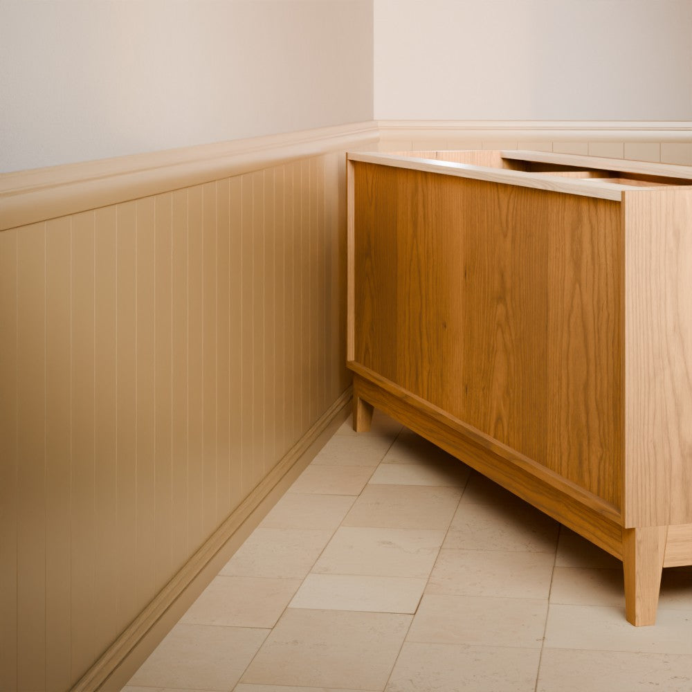 A light natural wood vanity cabinet with a matching wood countertop, shown in a bathroom corner with beige wainscoting and light tile flooring.