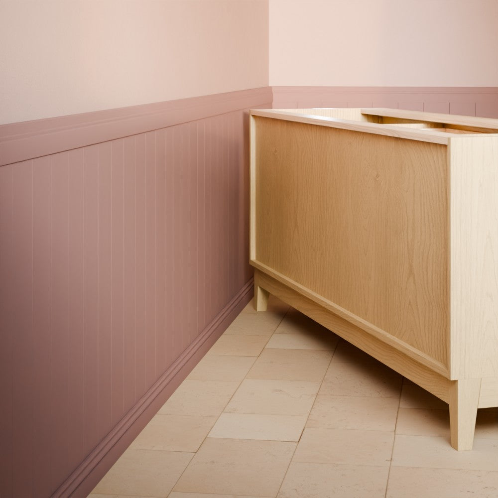 A light natural wood sideboard cabinet in the corner of a room with dusty pink wainscoted walls and beige tiled flooring.