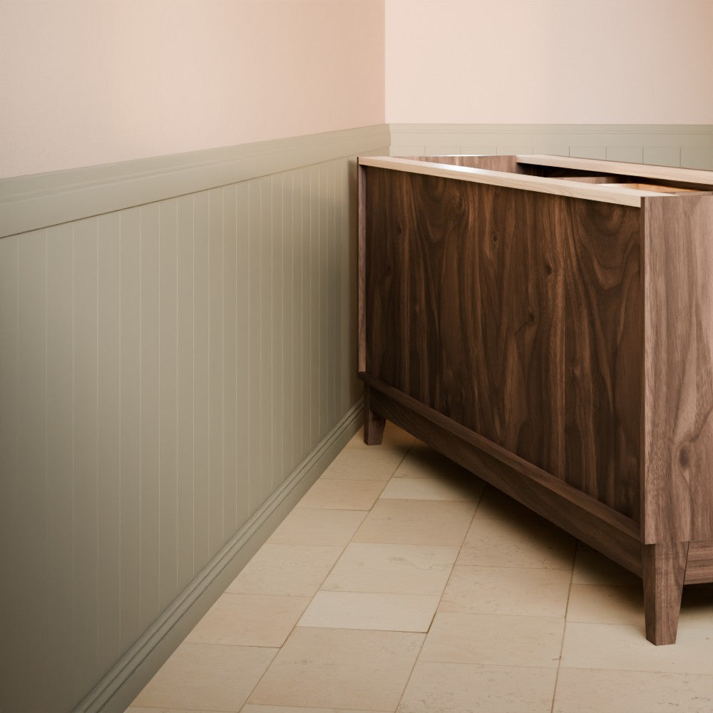A dark brown wooden vanity cabinet with a light beige countertop, shown in a bathroom corner with beige tile flooring and sage green wainscoting.