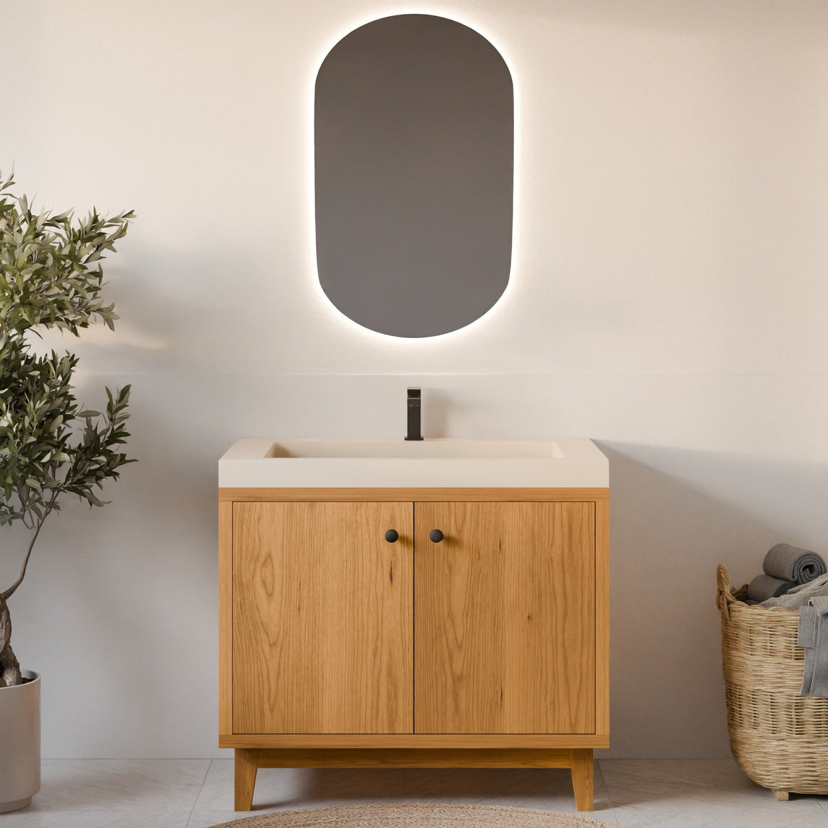 A modern bathroom vanity with a light oak wood cabinet, a white integrated sink countertop, and a matte black faucet. Above it is an oval backlit mirror with a soft white glow.