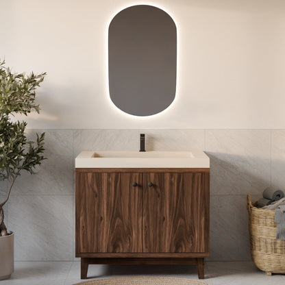 A modern bathroom vanity with a dark wood cabinet, a cream-colored countertop and basin, a matte black faucet, and an oval backlit mirror mounted on a light beige wall. The scene is styled with a potted plant on the left and a woven basket on the right.