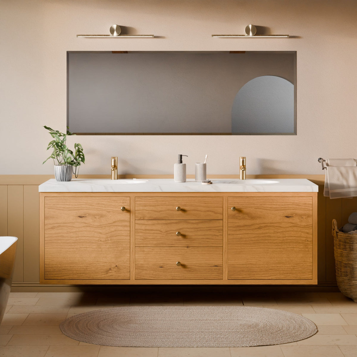 A modern floating bathroom vanity with a light oak wood cabinet, white marble countertop, and gold faucets, shown in a styled bathroom setting with a large mirror, wall sconces, and a woven rug.