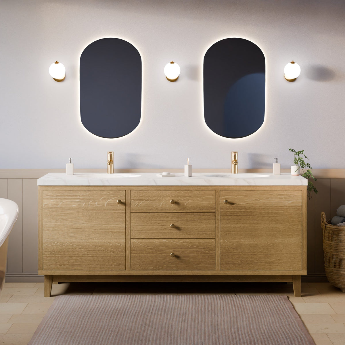 A modern double-sink bathroom vanity with a light oak wood cabinet, white marble tops, and gold hardware, set against a neutral gray wall with two oval backlit mirrors and wall sconces.#wood_white-oak
