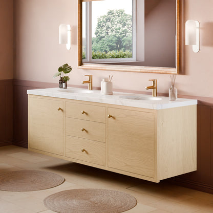 A modern double-sink bathroom vanity with a light oak wood cabinet, white marble countertop, and gold faucets, shown in a styled bathroom setting with a mirror, wall sconces, and woven rugs.