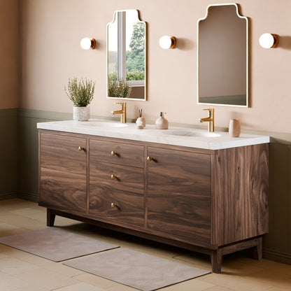 A modern double-sink bathroom vanity with a dark wood cabinet, white marble countertop, and gold fixtures, shown in a styled bathroom setting with two mirrors, wall sconces, and bath mats.