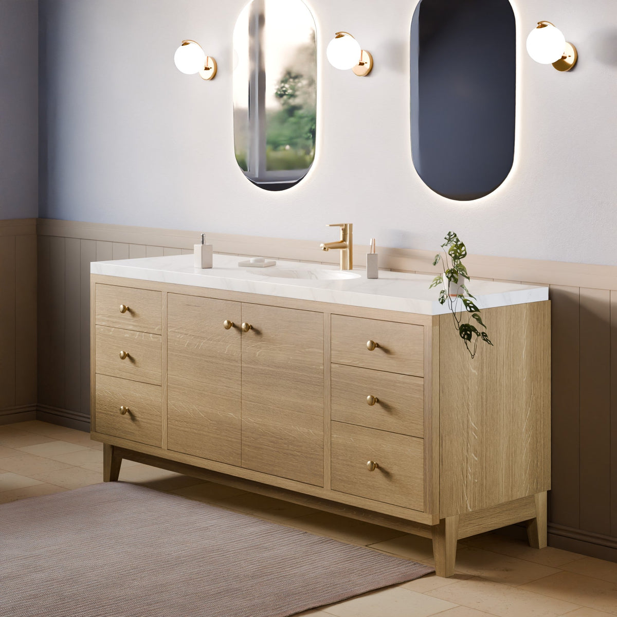 A modern double-sink bathroom vanity in light oak wood with a white countertop, brass hardware, and a gold faucet, shown in a styled bathroom setting with mirrors, wall sconces, and a rug.