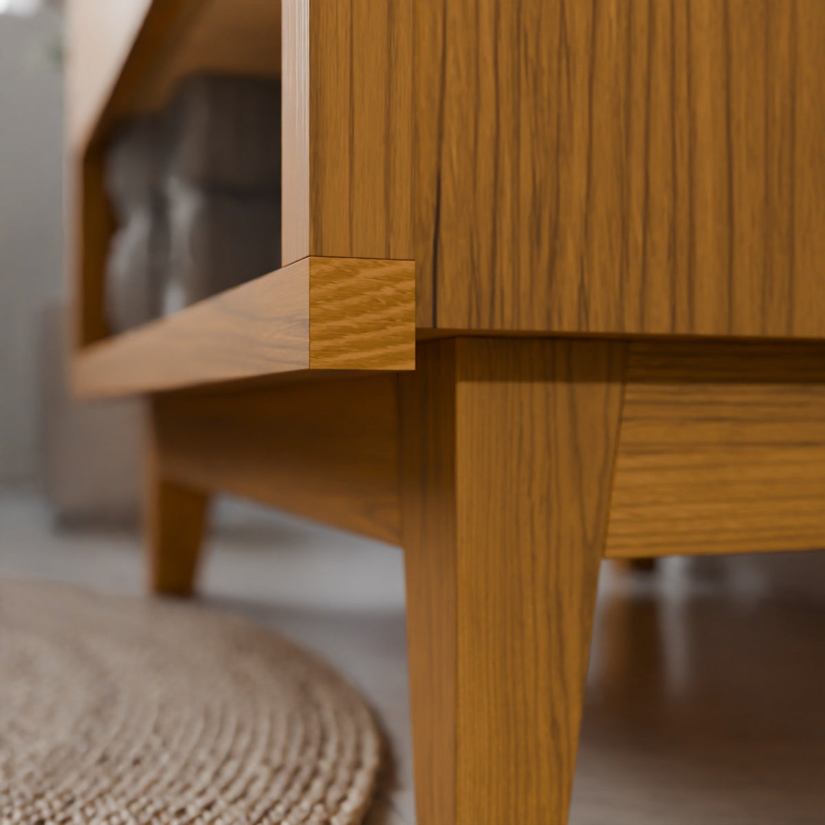 Close-up of a mid-century modern wooden coffee table with a warm oak finish, showing the corner joint and leg detail in a softly blurred living room setting.