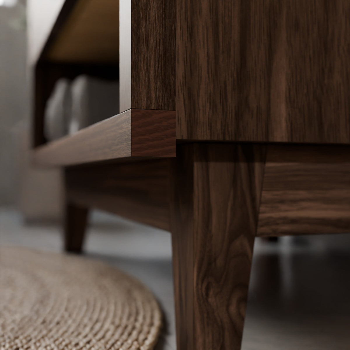 Close-up of a dark brown wooden furniture piece, showing the grain of the wood on the leg and side panel, with a blurred woven rug on the floor.