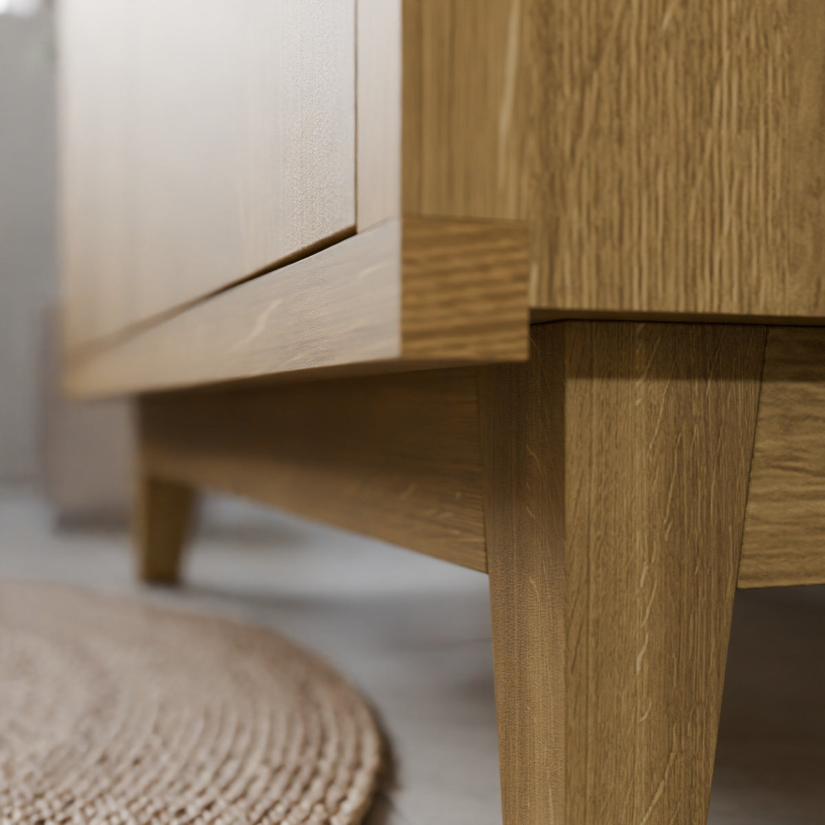 Close-up of a light oak wood furniture piece, showing the grain, leg, and baseboard detail in a modern room setting.