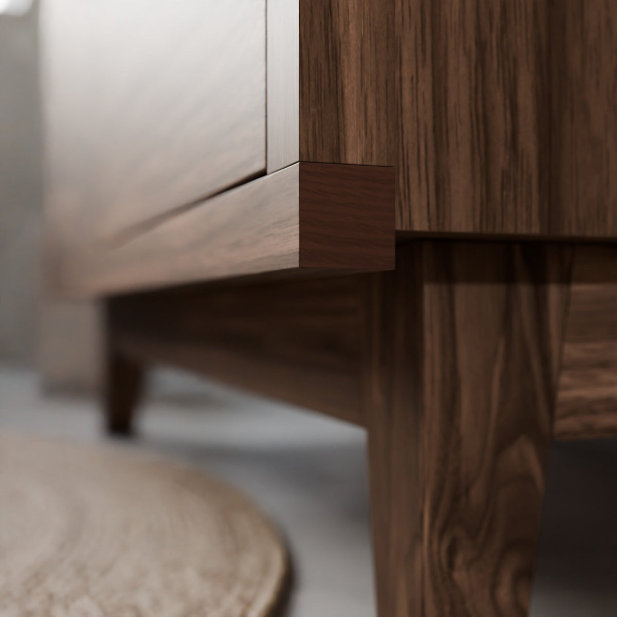 Close-up of a dark brown wooden furniture piece, showing the corner joint and leg with a light-colored wall and floor in the background.