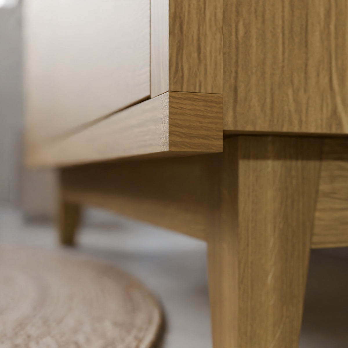 Close-up of a light oak wood furniture piece showing the corner joint and leg detail, with a blurred neutral background.