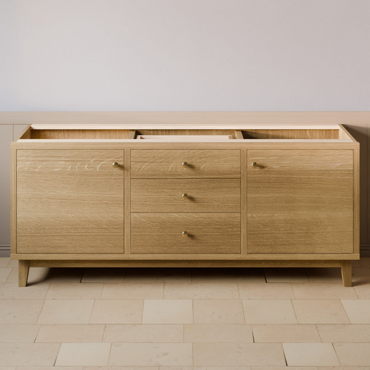 A light oak wood sideboard or credenza with three drawers in the center and two larger cabinet doors on the sides, finished with small brass handles and tapered legs, shown against a neutral wall and tiled floor.#wood_white-oak