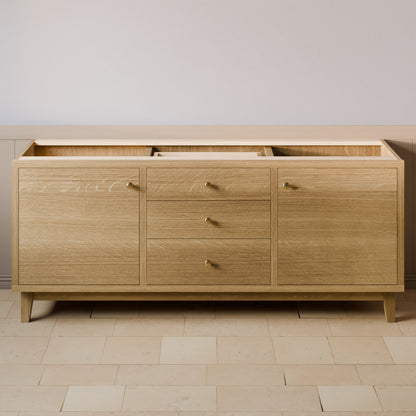 A light oak wood sideboard or credenza with three drawers in the center and two larger cabinet doors on the sides, finished with small brass handles and tapered legs, shown against a neutral wall and tiled floor.