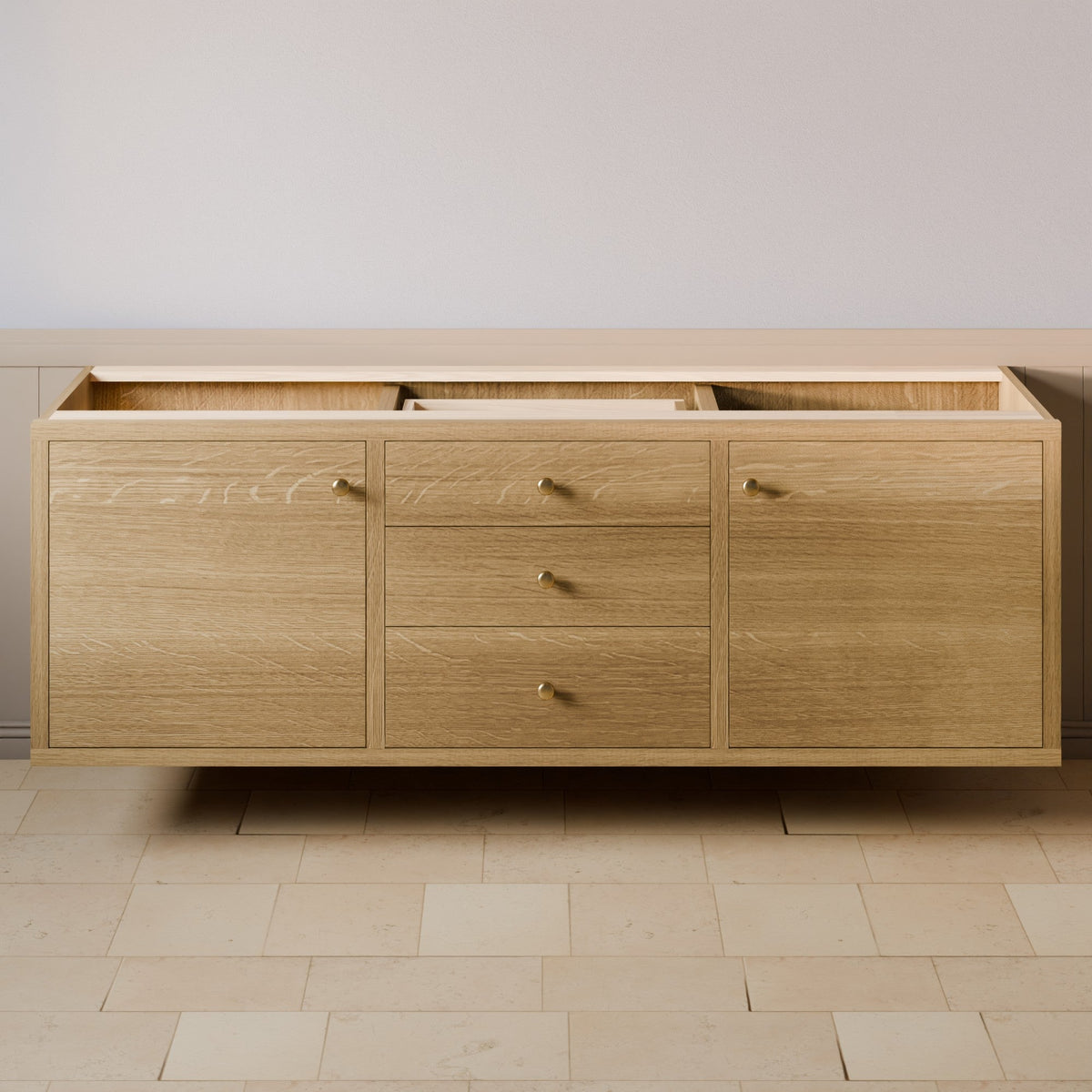 A floating wooden sideboard or cabinet with three drawers in the center and two larger doors on the sides, finished in light oak wood with small round brass handles, shown against a neutral beige wall and tiled floor.