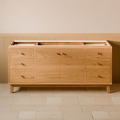 A light oak wood sideboard or credenza with six drawers and two cabinet doors, featuring small brass handles and tapered legs, set against a beige wall with wainscoting and light stone tile flooring.