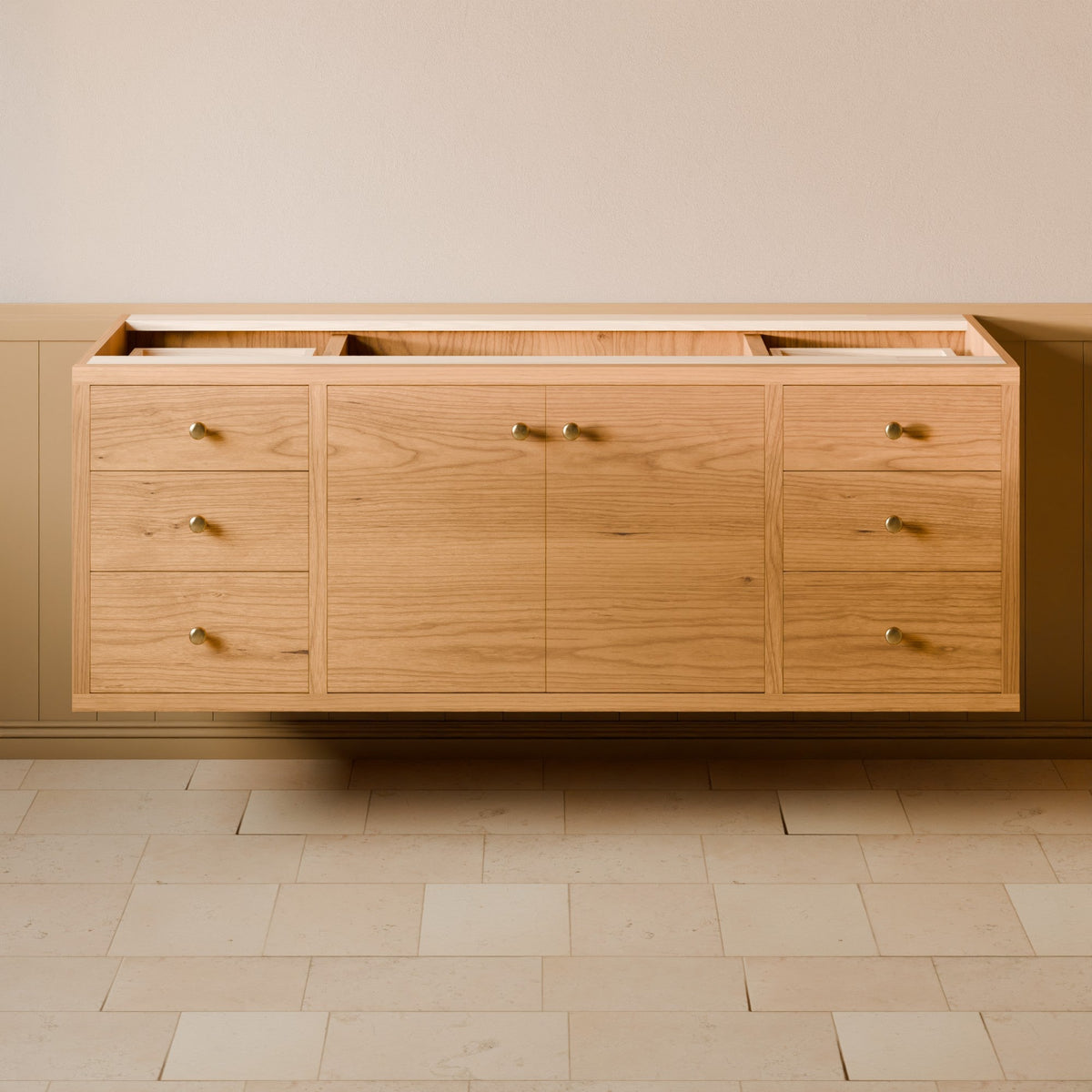 A light oak wood wall-mounted storage cabinet with multiple drawers and doors, featuring small brass handles, set against a beige wall and light stone tile floor.