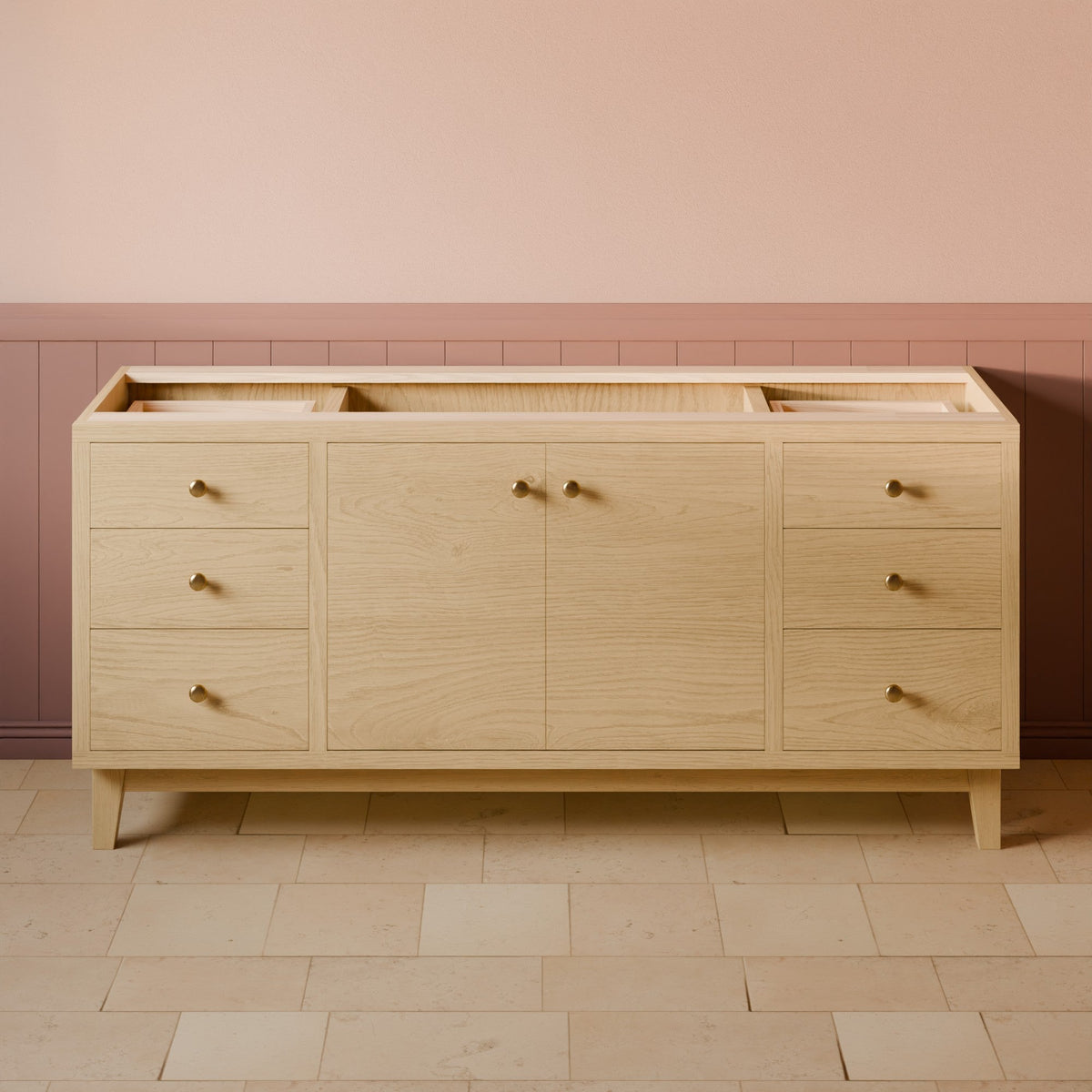 A light natural oak bathroom vanity or sideboard with six drawers, two central doors, and brass handles, set against a pink and brown wainscoted wall and tiled floor.