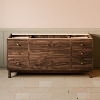 A mid-century modern wooden sideboard or credenza with a dark walnut finish, featuring multiple drawers and cabinet doors with small brass knobs, set against a beige wall and tiled floor.
