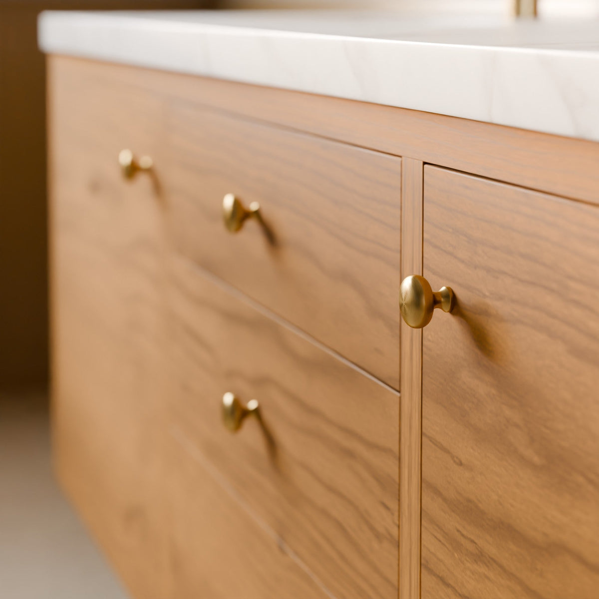 Close-up of a wooden vanity cabinet with three drawers and one door, featuring round brass knobs and a white marble countertop.