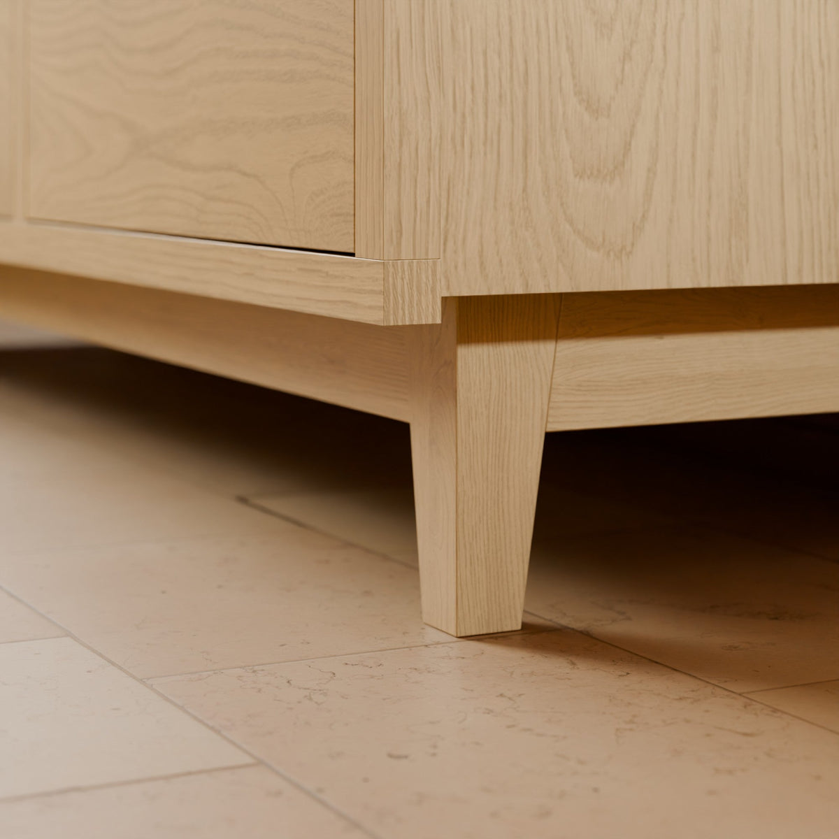 Close-up of a light natural oak wooden furniture piece, showing the grain, joint construction, and leg on a beige tiled floor.#wood_maple