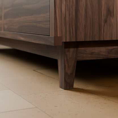 Close-up of a dark wood cabinet or sideboard with a visible leg, shown in a real interior setting on a light stone tile floor.