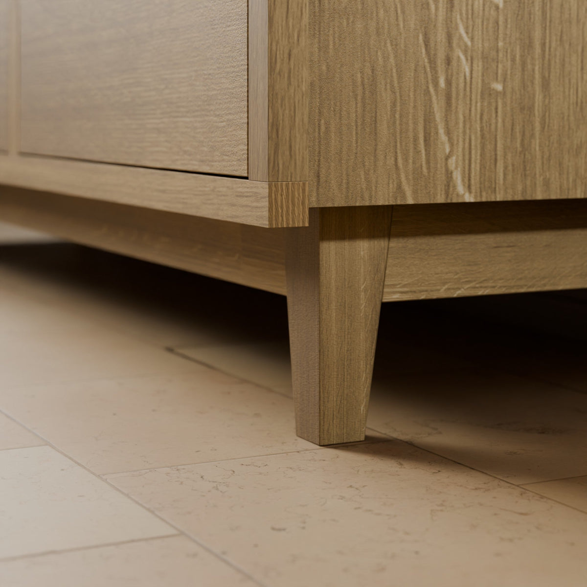 Close-up detail of a light oak wood furniture piece, showing the corner joint, drawer front, and tapered leg resting on a beige tiled floor.#wood_white-oak