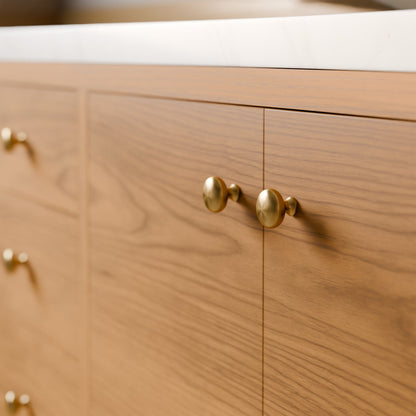 Close-up of a wooden cabinet with two doors and round brass knobs, set against a white countertop.