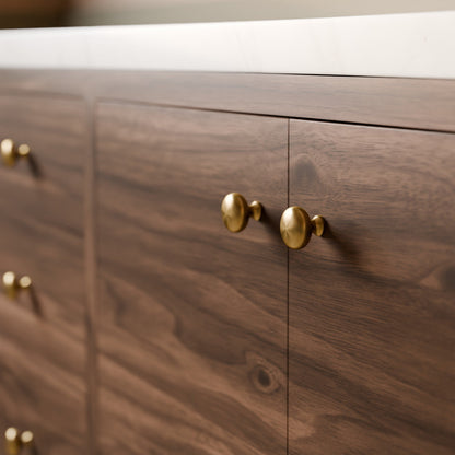 Close-up of a dark wood cabinet with round brass knobs and a white countertop edge.