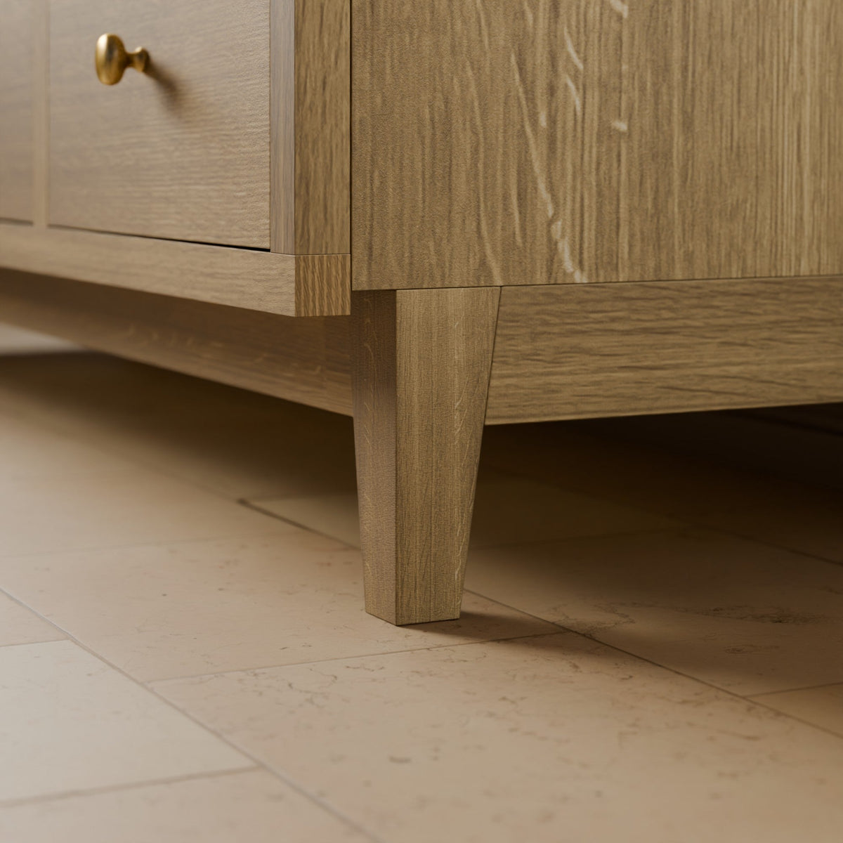 Close-up of a light oak wood cabinet or sideboard showing a drawer with a brass knob, the cabinet leg, and the tiled floor below.