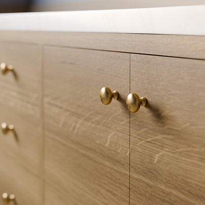 Close-up of a light oak wood cabinet with round brass knobs and a white countertop.