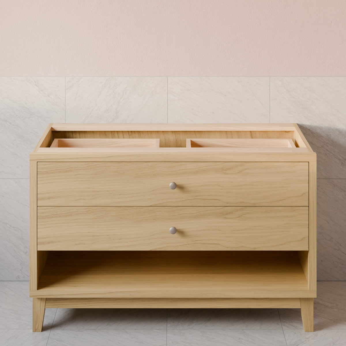 A light natural wood changing table or vanity with two drawers and a lower open shelf, shown against a pale pink and light gray tiled wall.