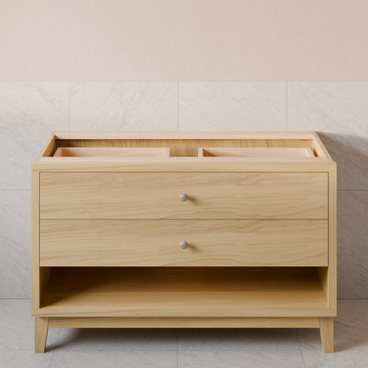 A light natural wood changing table or vanity with two drawers and a lower open shelf, shown against a pale pink and light gray tiled wall.
