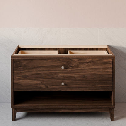 A dark brown wooden bathroom vanity cabinet with two drawers, round silver knobs, and an open lower shelf, set against a light gray marble-tiled wall and pale pink upper wall.