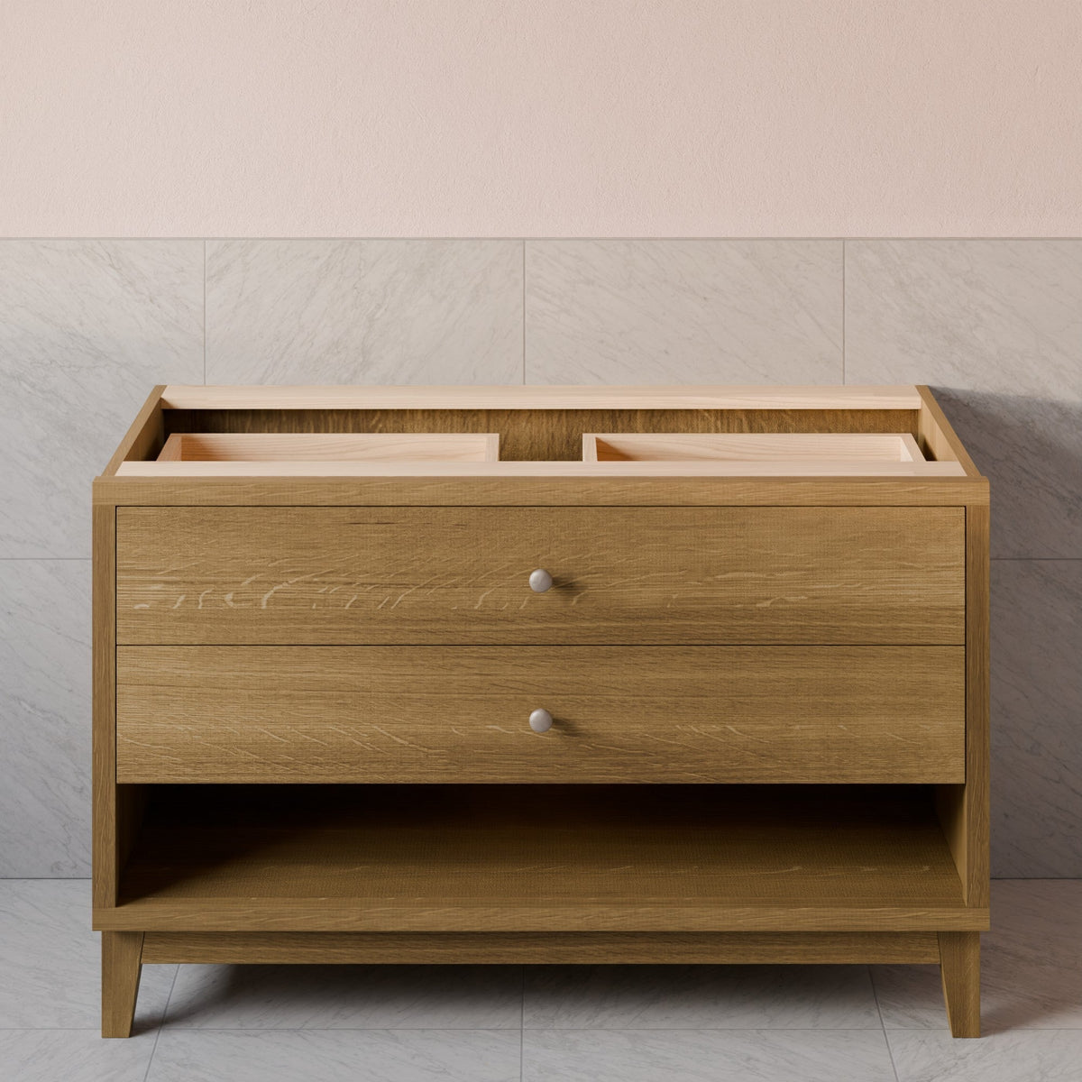 A Krovel Furniture Co. light oak wood bathroom vanity cabinet with two drawers, a lower open shelf, and a hinged top section that is open to reveal storage compartments. The cabinet features two small round silver knobs and is set against a neutral tiled wall background.