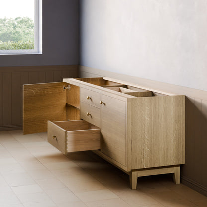 A light oak wood sideboard or credenza with brass drawer pulls, shown in a room setting with one drawer open and the top surface lifted open. The room features a window, paneled lower wall, and light-colored tile floor.