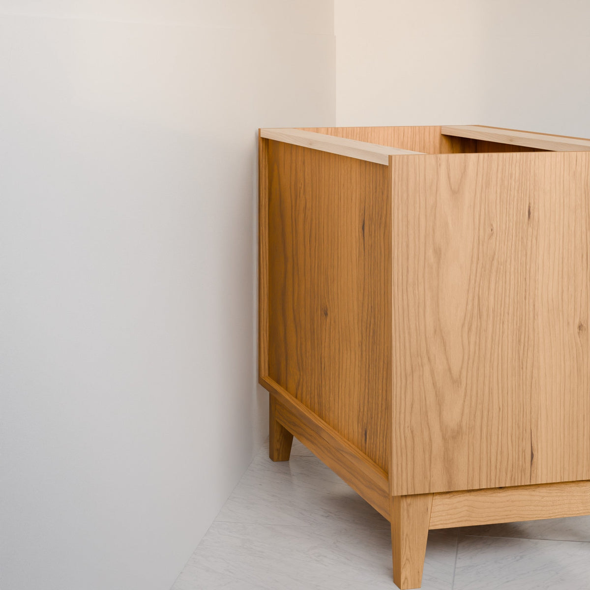 A light natural oak wooden cabinet or storage unit shown in a minimalist corner setting with off-white walls and a light gray floor.