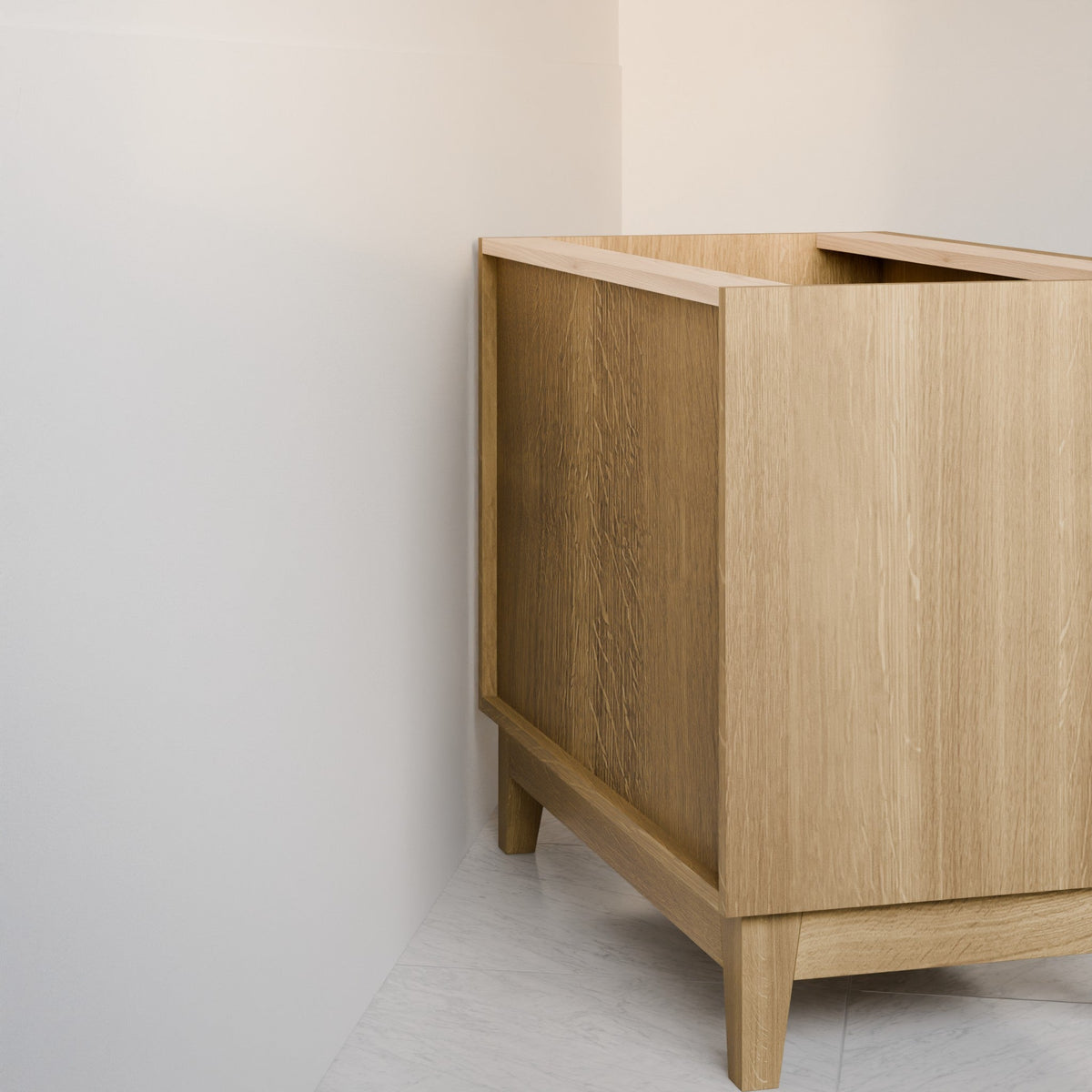 A close-up of a light oak wood vanity cabinet corner, showing the natural wood grain, clean lines, and tapered legs in a minimalist room corner.