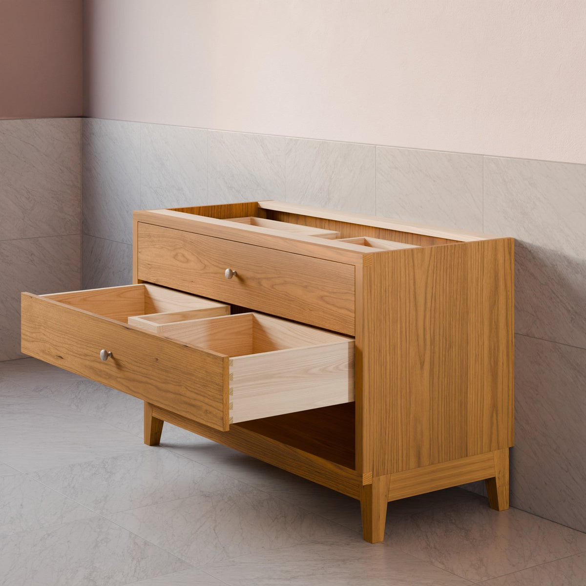 A light oak wood storage cabinet with two drawers, one of which is open to show interior compartments, set against a tiled wall and floor.