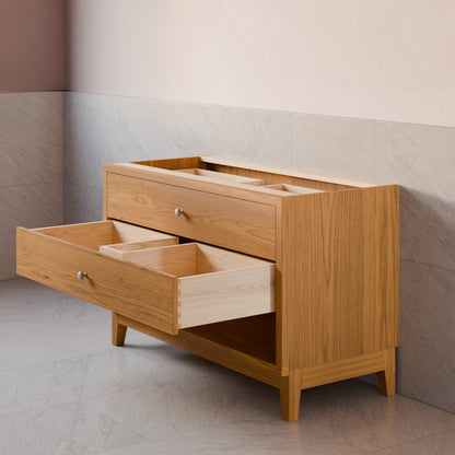 A light oak wood storage cabinet with two drawers, one of which is open to show interior compartments, set against a tiled wall and floor.