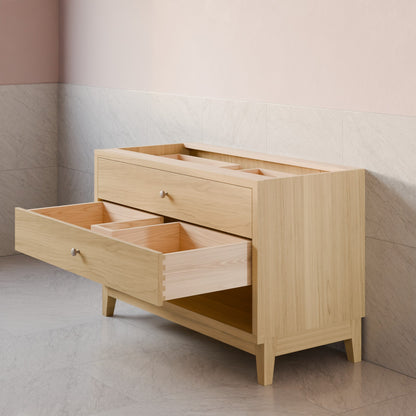 A light natural wood storage cabinet with two open drawers and a top organizer tray, set against a two-tone beige and gray tiled wall.